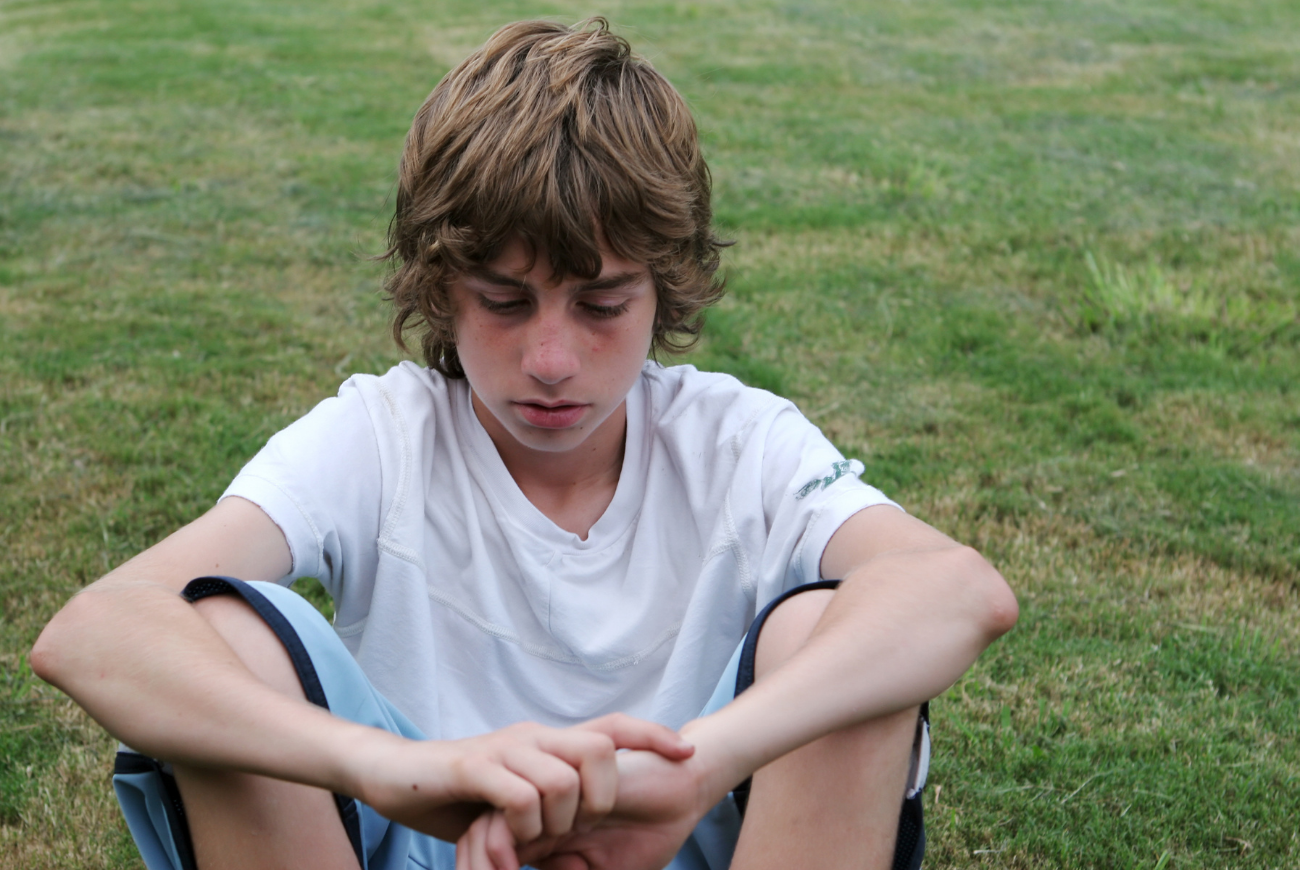 young male teen sitting on lawn looking down learning how to deal with puberty mood swings