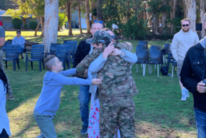 boy wearing veteran mentors army uniform hugs family tightly